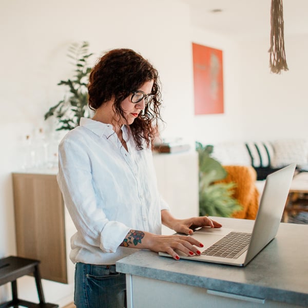 Kvinna står med laptop vid en bänk i hemmamiljö