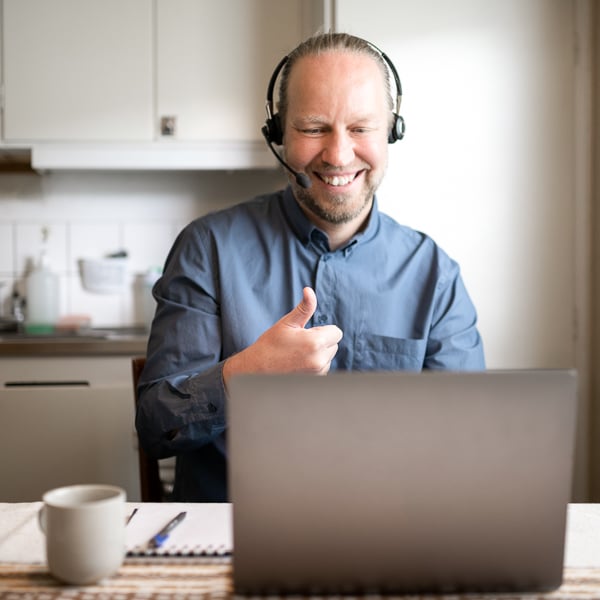 Man med ett headset gör tummen upp framför en laptopa