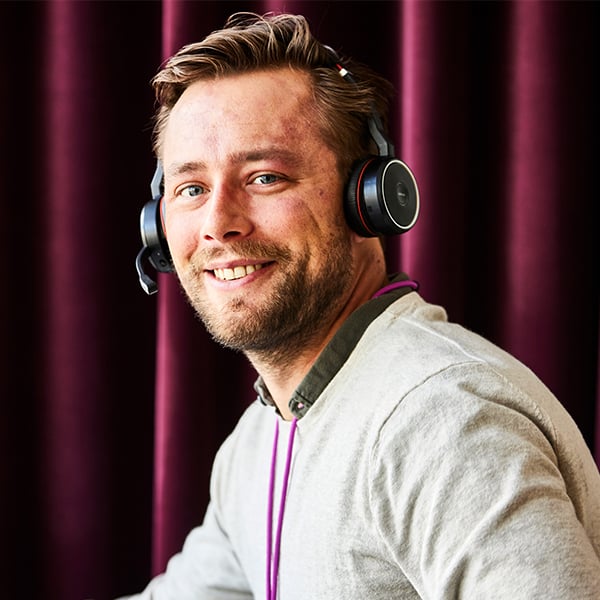 Man med ett headset på sig ler in i kameran 