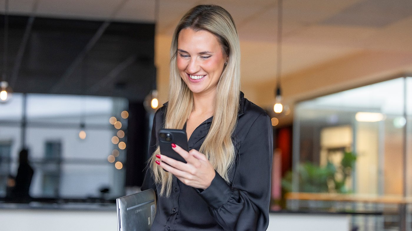 Kvinnlig medarbetare som ler när hon tittar på sin mobiltelefon