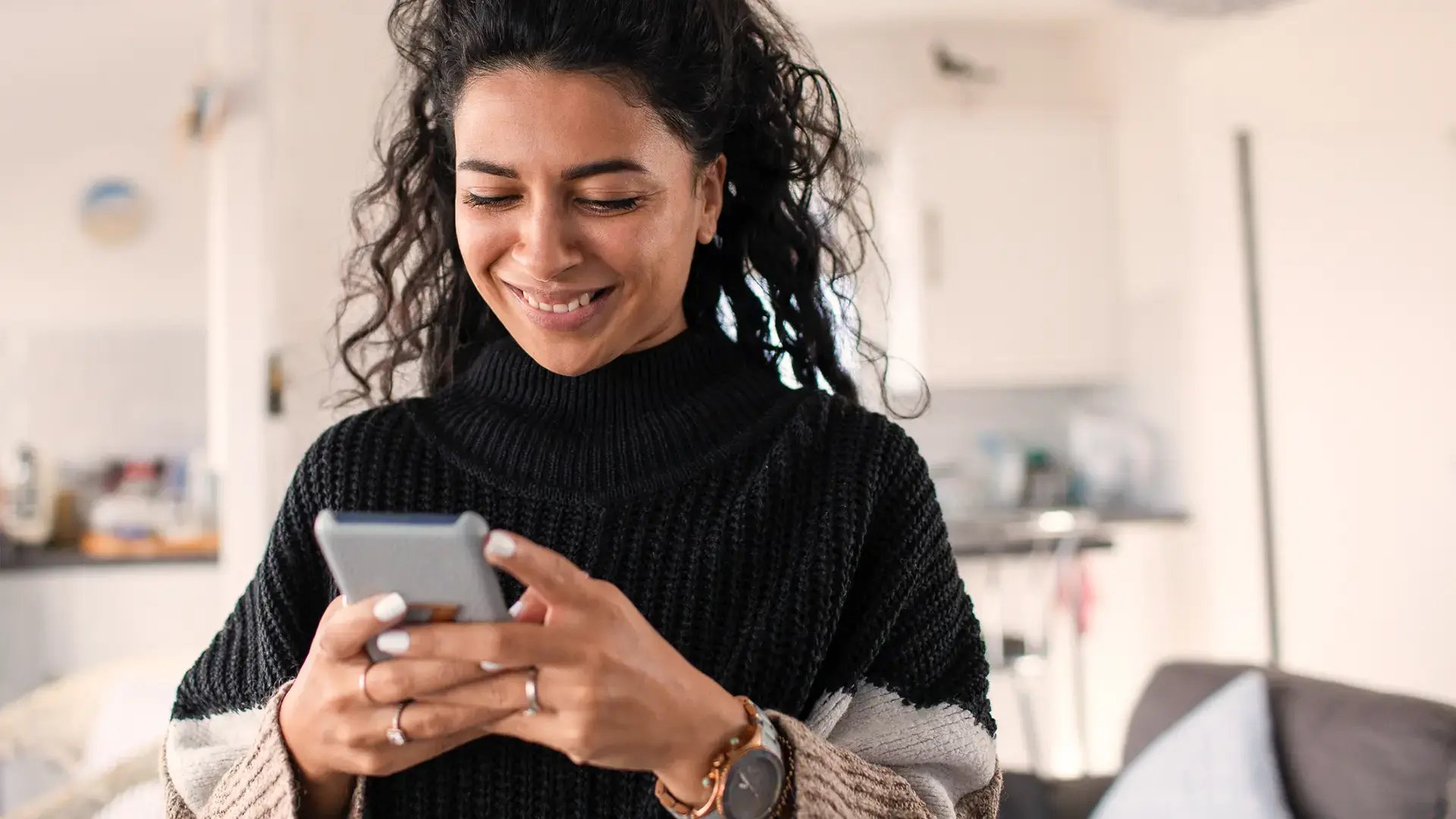 Kvinna ler medan hon tittar ner i en mobil