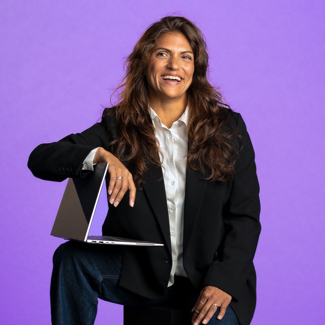 Leende kvinna med laptop under armen mot en lila bakgrund