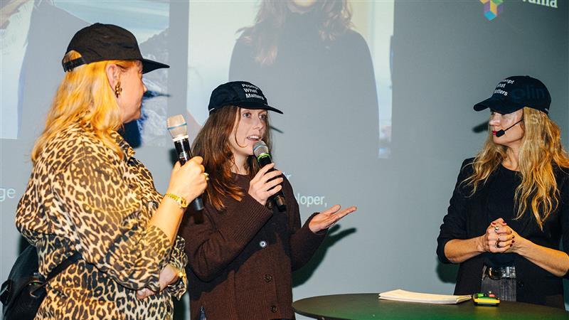 Tre personer på scenen pratar i mikrofoner under ett event.