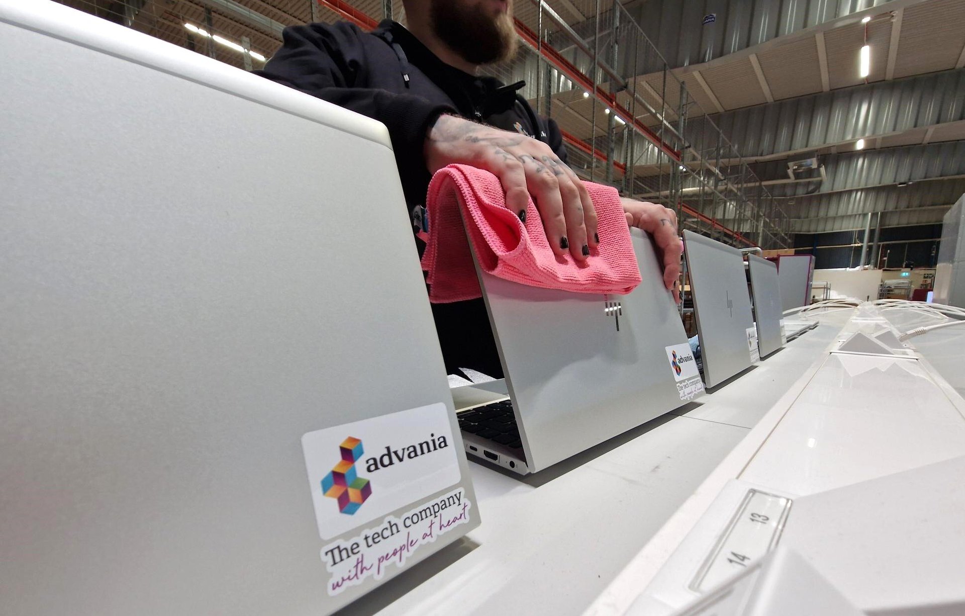 En person torkar rent en rad bärbara datorer med rosa trasa. Alla datorer har Advanias logotyp och slogan: “The tech company with people at heart”.